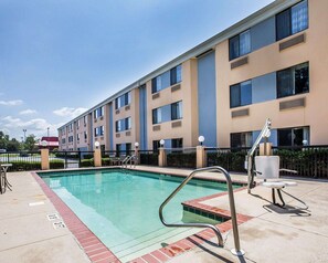 A hotel pool area with a clear pool, a metal pool ladder, and a fence.