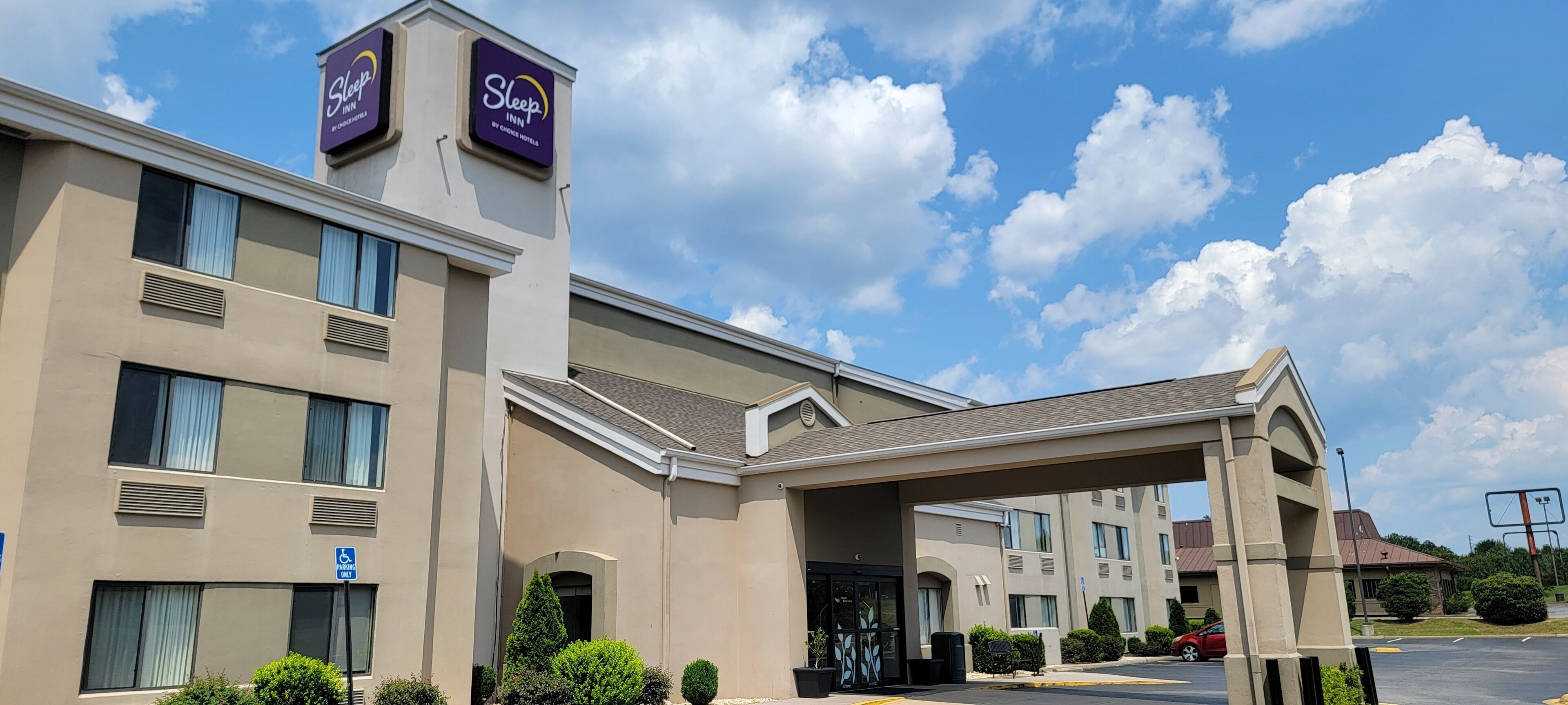 A Sleep Inn hotel with a parking lot, a covered entrance, and a clear blue sky with clouds.