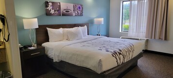 Habitación de hotel con cama, dos lámparas de noche, mesita de noche, teléfono en la pared y ventana con cortinas.