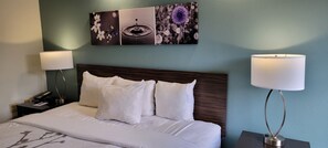 A neatly made bed with white linens and pillows, a wooden headboard, and a wall-mounted artwork above it.