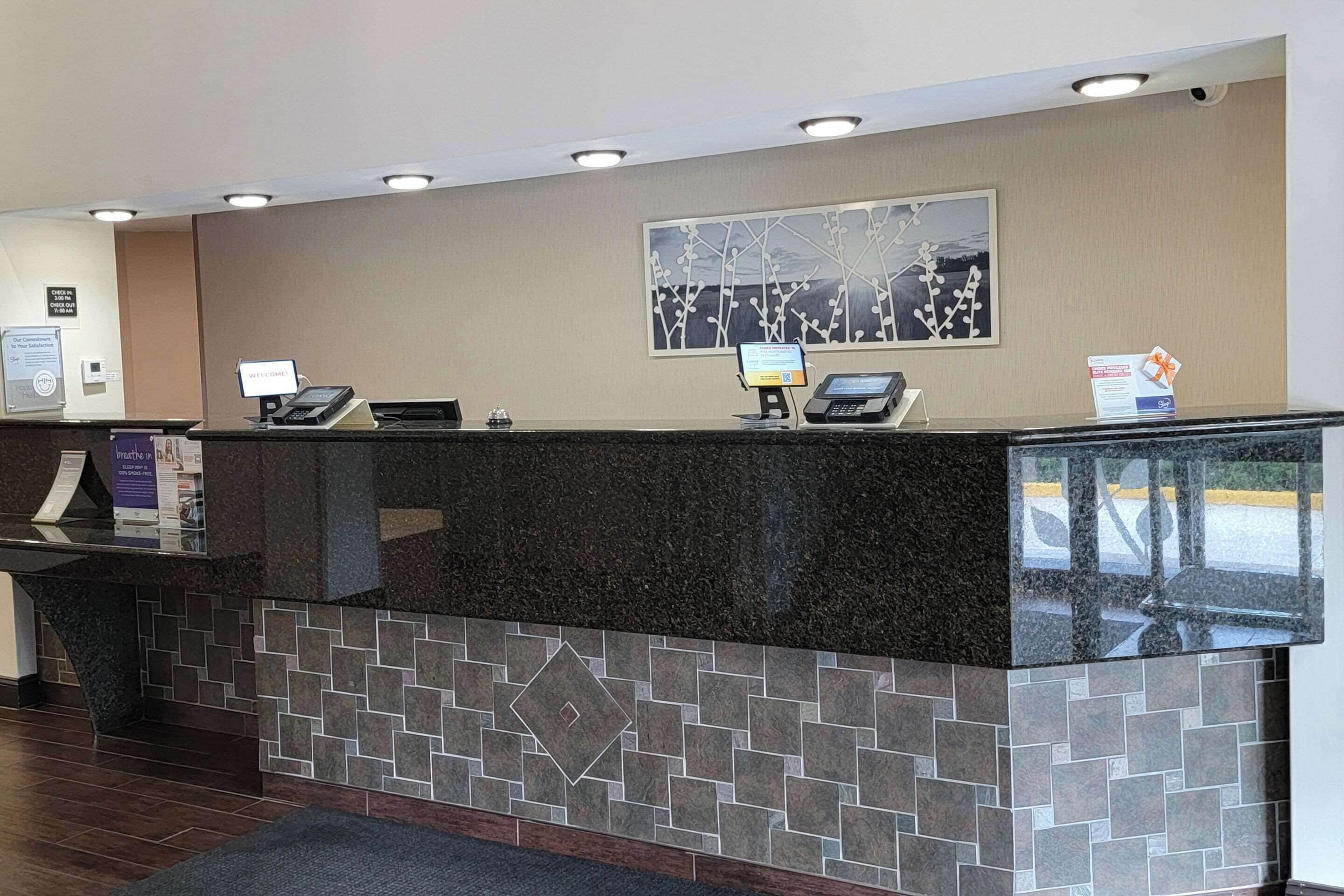 A reception desk with a digital screen, a telephone, and a sign indicating a check-in area.
