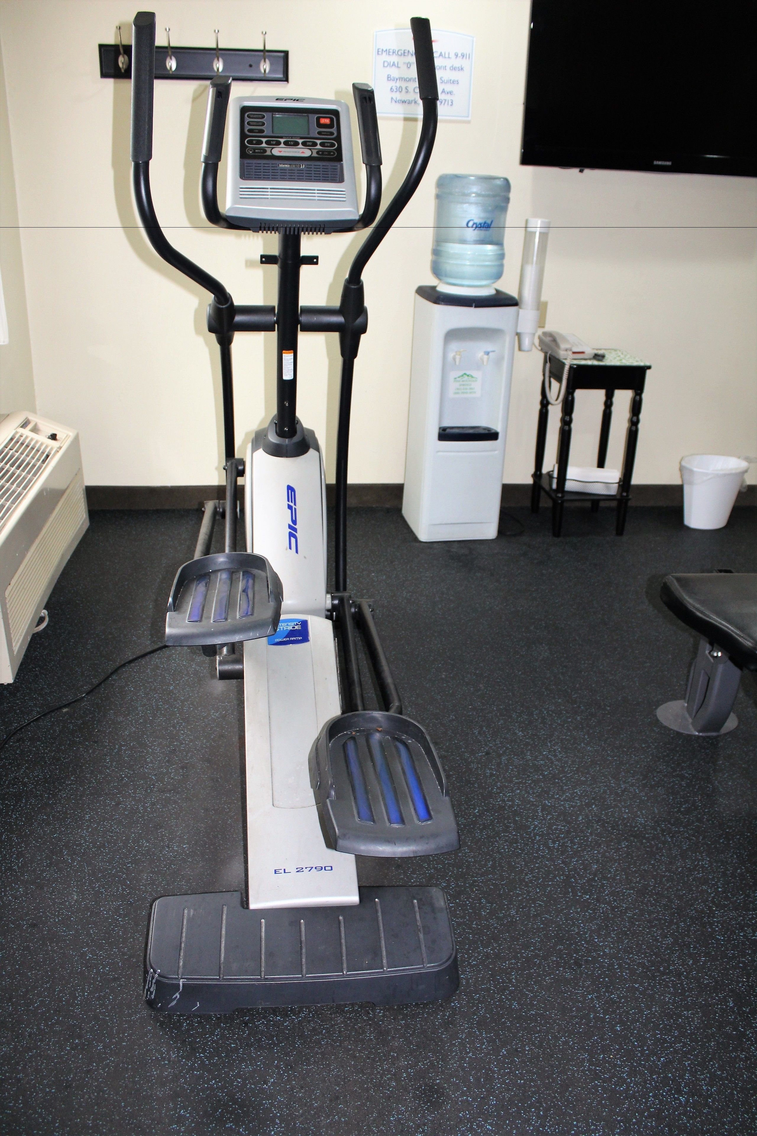 An exercise machine with a digital display, a water dispenser, and a chair in a room with a black floor.