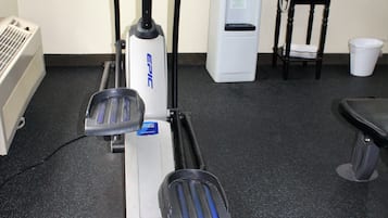 An exercise machine with a digital display, a water dispenser, and a chair in a room with a black floor.