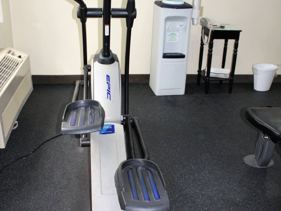 An exercise machine with a digital display, a water dispenser, and a chair in a room with a black floor.