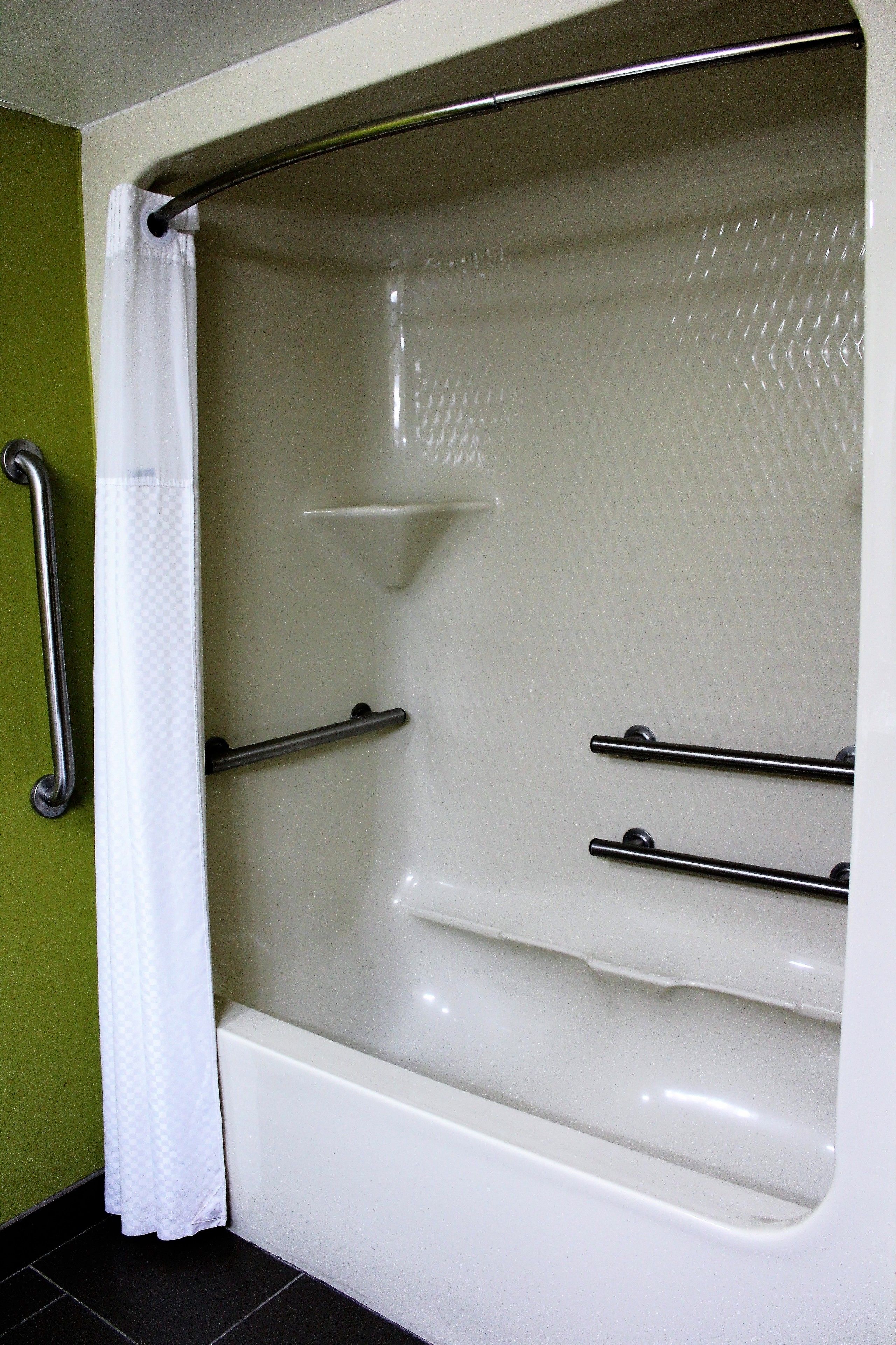 A bathtub with a shower curtain, grab bars, and a shelf.