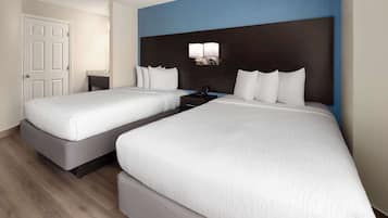 A hotel room with two beds, a nightstand, a desk, and a wall-mounted lamp.