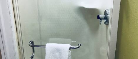 A shower stall with a white towel hanging on a metal rack, a showerhead, and a door handle.