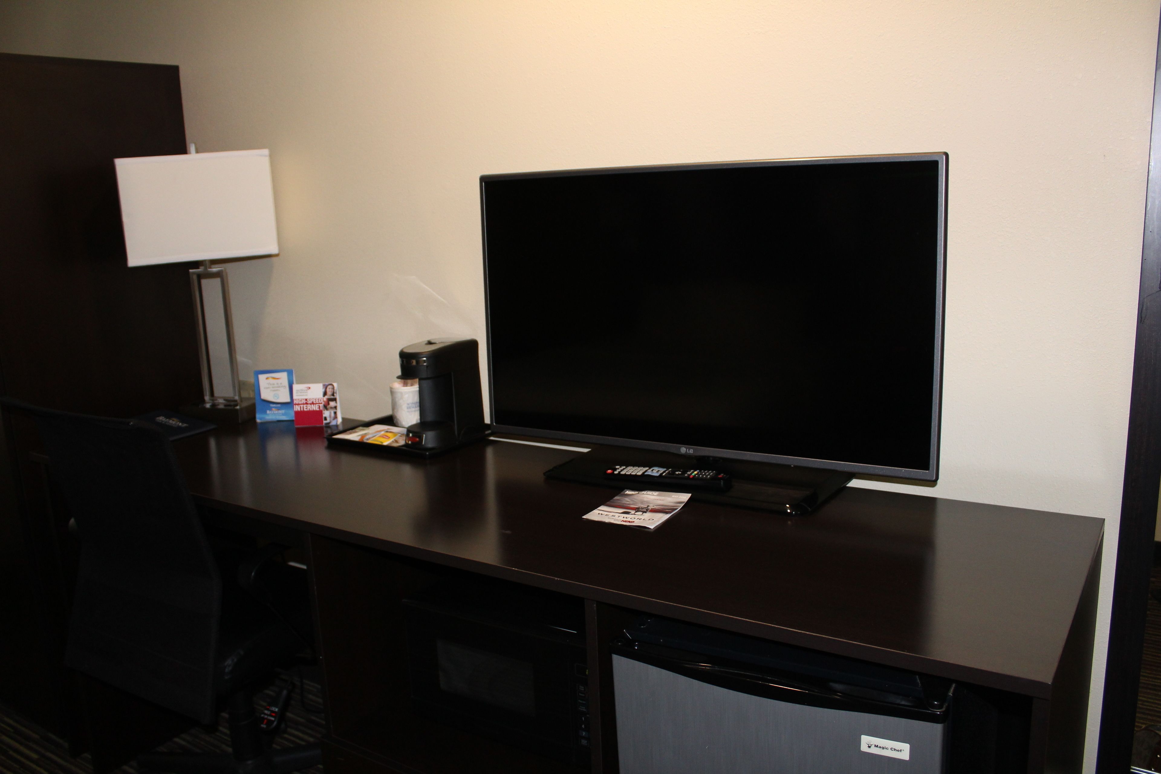 A hotel room with a flat-screen TV, a coffee maker, a remote control, and a small table with a magazine.