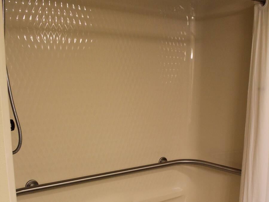 A shower with a grab bar, a drain, and a curtain.