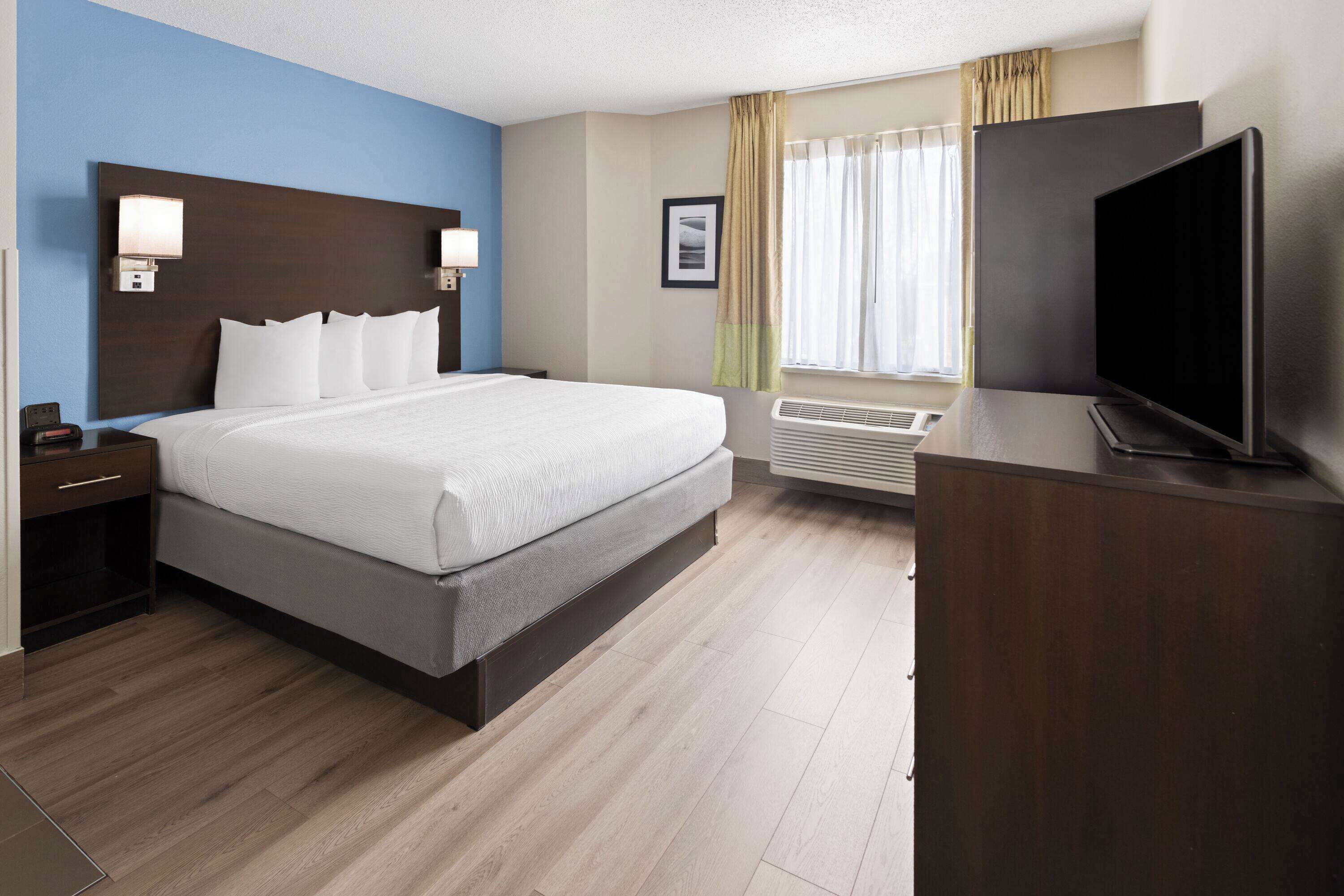 Habitación de hotel con una cama grande, mesitas de noche, un televisor de pantalla plana, una ventana con cortinas y un equipo de aire acondicionado instalado en la pared.