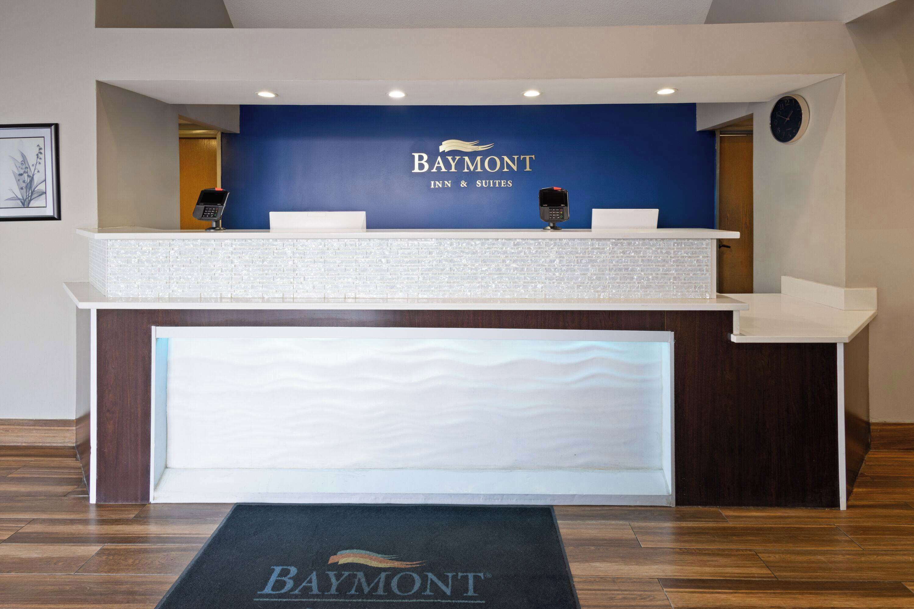 A Baymont Inn & Suites reception desk with a blue wall, a clock, and a digital keypad.