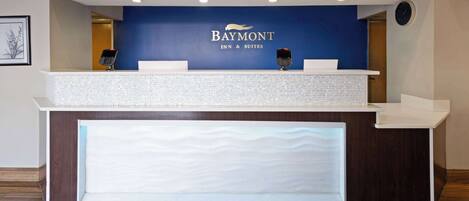 A Baymont Inn & Suites reception desk with a blue wall, a clock, and a digital keypad.