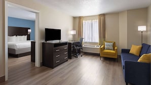 Habitación de hotel con cama, escritorio con televisor, silla, sofá y ventana con cortinas.