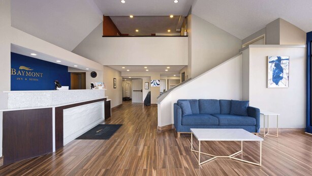Un hall de hotel con una recepción, un sofá azul, una escalera y un suelo de madera.