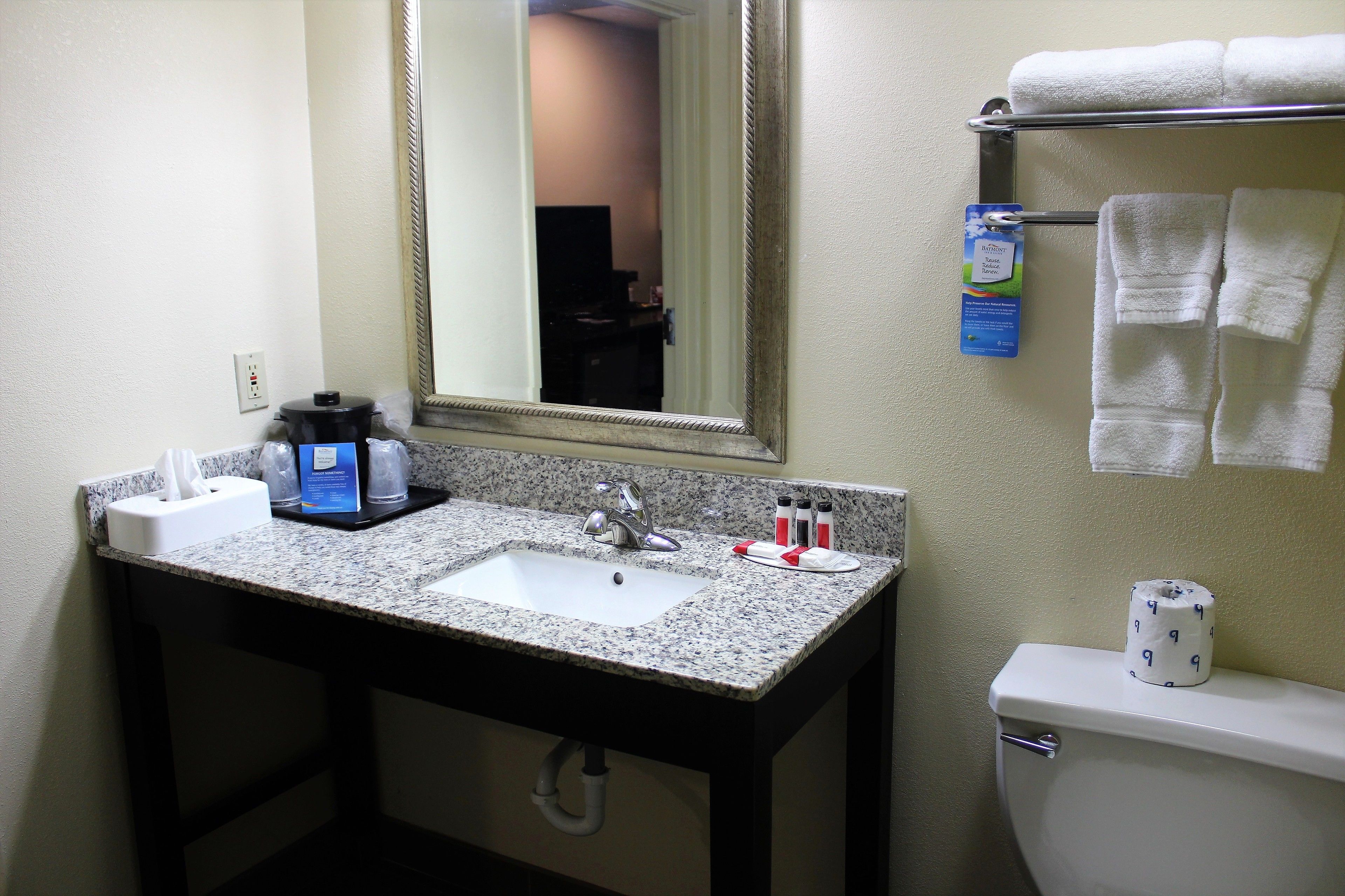 A bathroom with a granite countertop sink, a mirror, a towel rack, and a toilet.