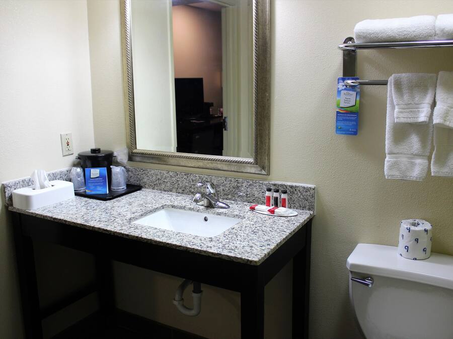 A bathroom with a granite countertop sink, a mirror, a towel rack, and a toilet.