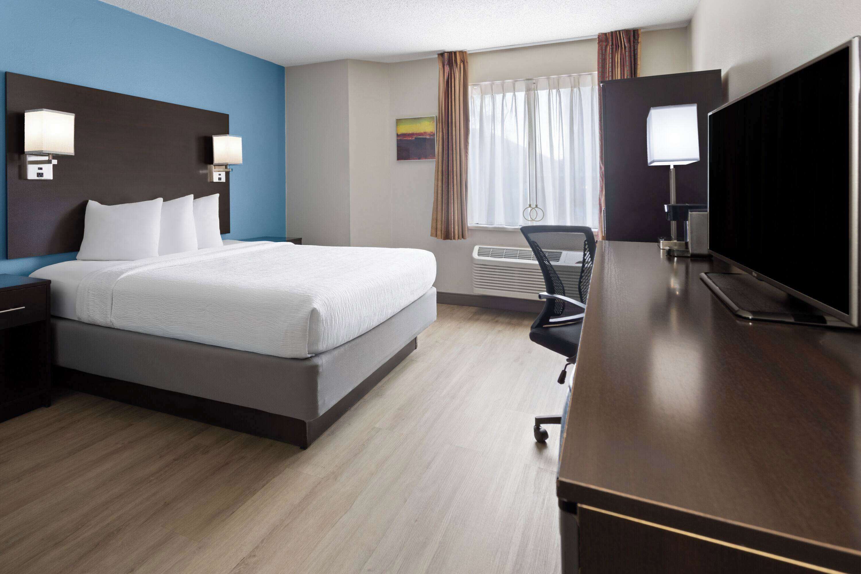 Habitación de hotel con una cama grande, un escritorio, una silla, un televisor y una ventana con cortinas.