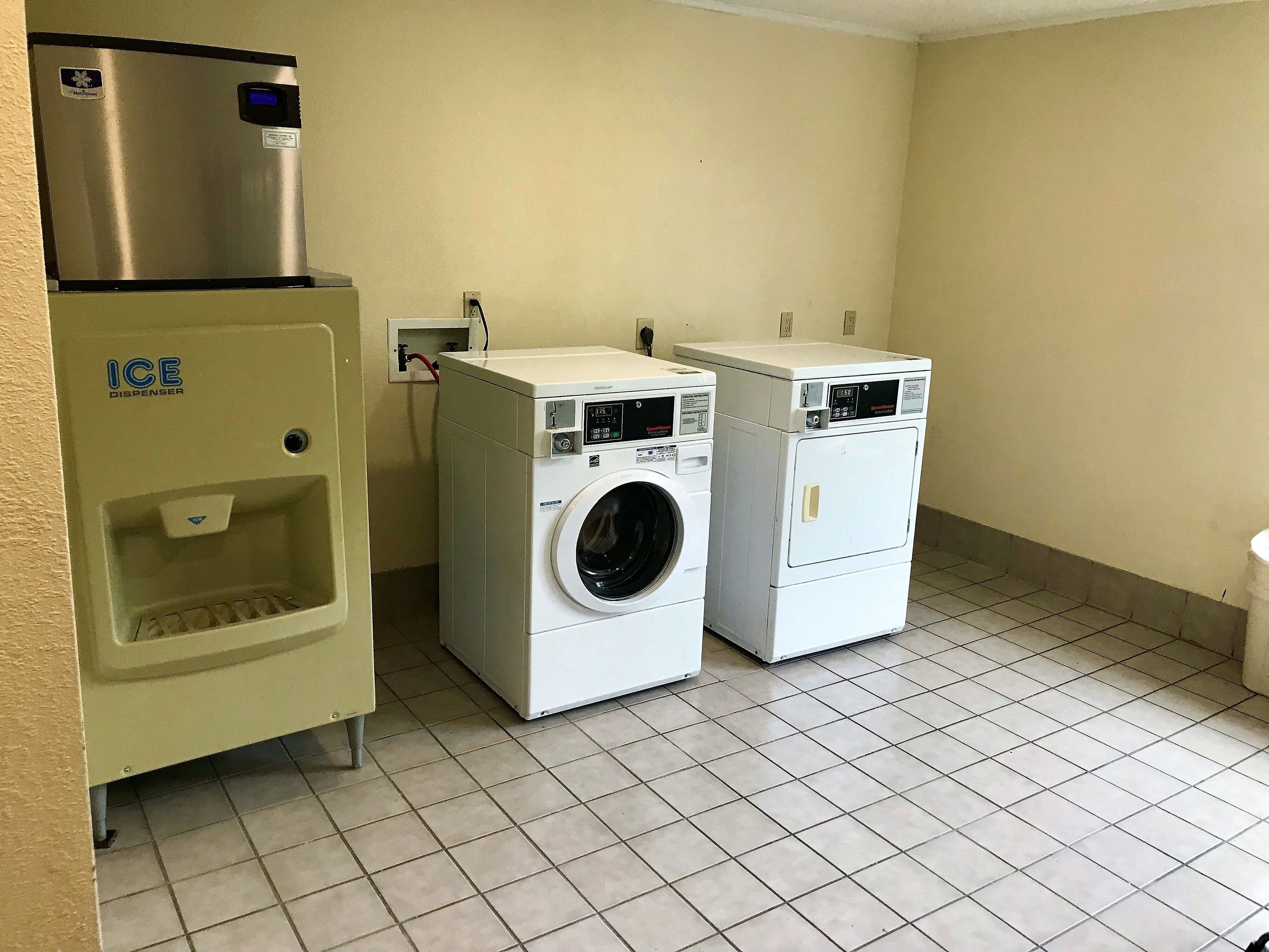 A laundry room with an ice dispenser, two washing machines, and a tiled floor.