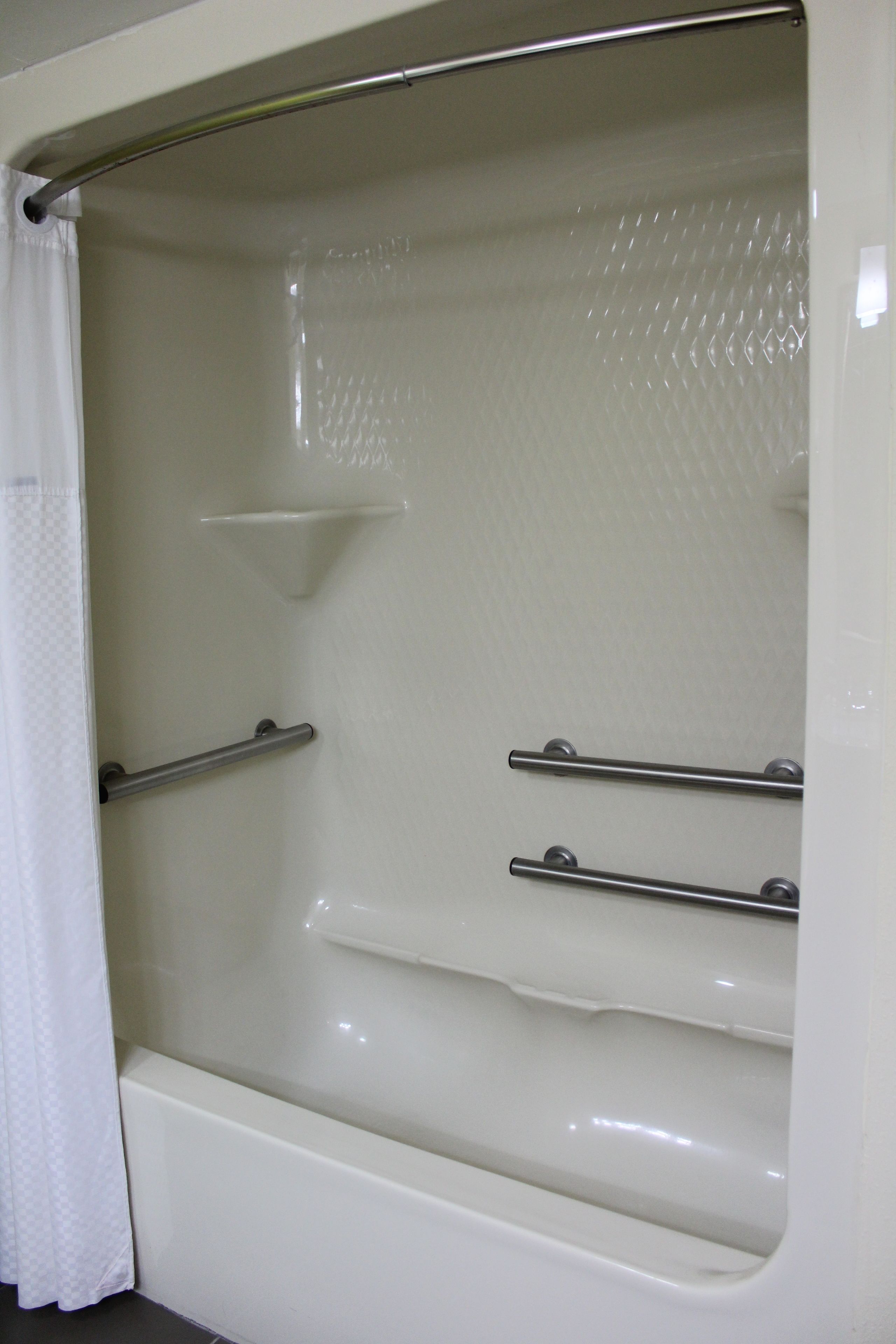 A white bathtub with a shower curtain, a grab bar, and a shelf.