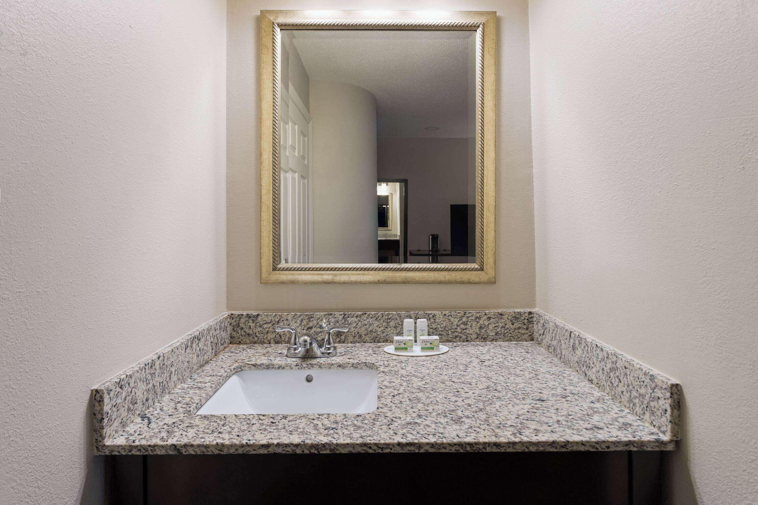 Une salle de bain avec un lavabo doté d’un plan de travail en granit, un grand miroir et une porte blanche en arrière-plan.