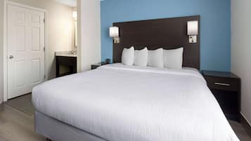 A hotel room with a large bed, a nightstand, a dresser, a bathroom with a sink and mirror, and a door.
