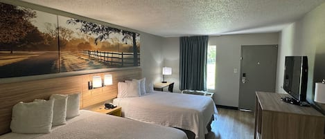 A hotel room with two beds, a desk, a television, and a painting on the wall.