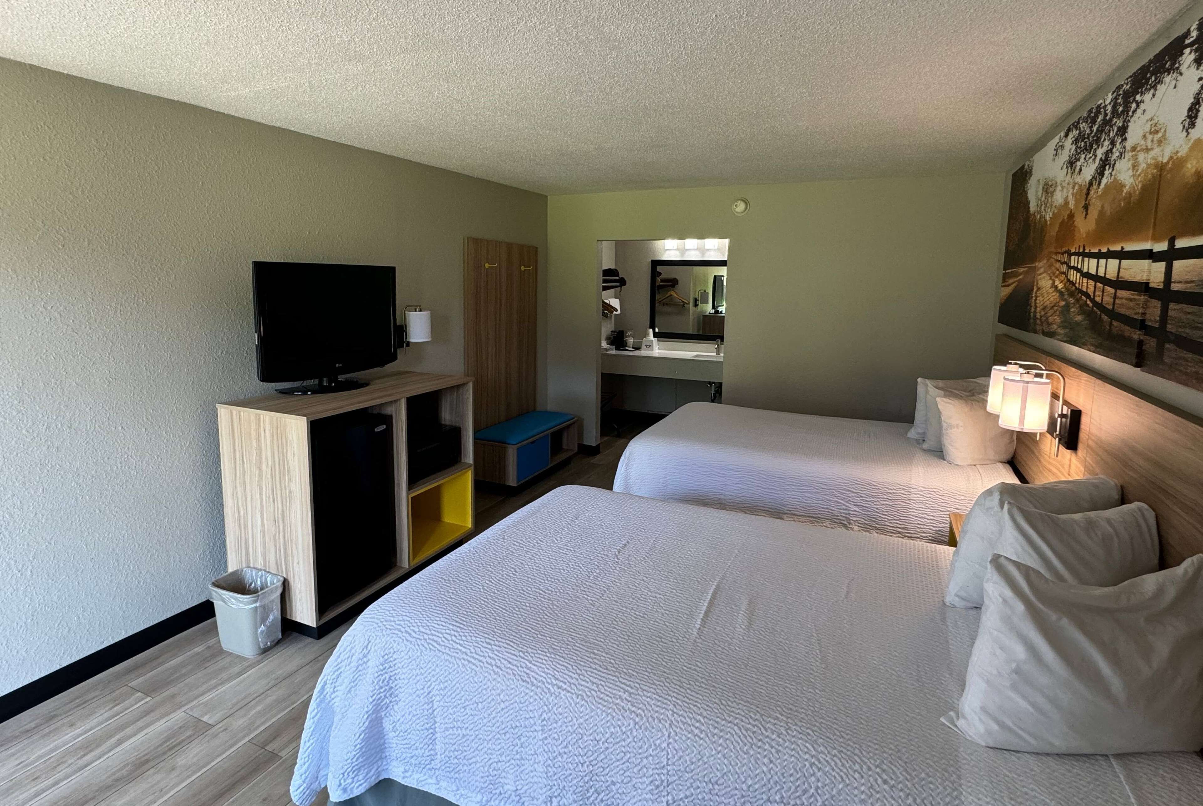 A hotel room with two beds, a TV, a desk, a mirror, and a painting on the wall.