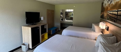 Habitación de hotel con dos camas, televisión, escritorio, espejo y un cuadro en la pared.