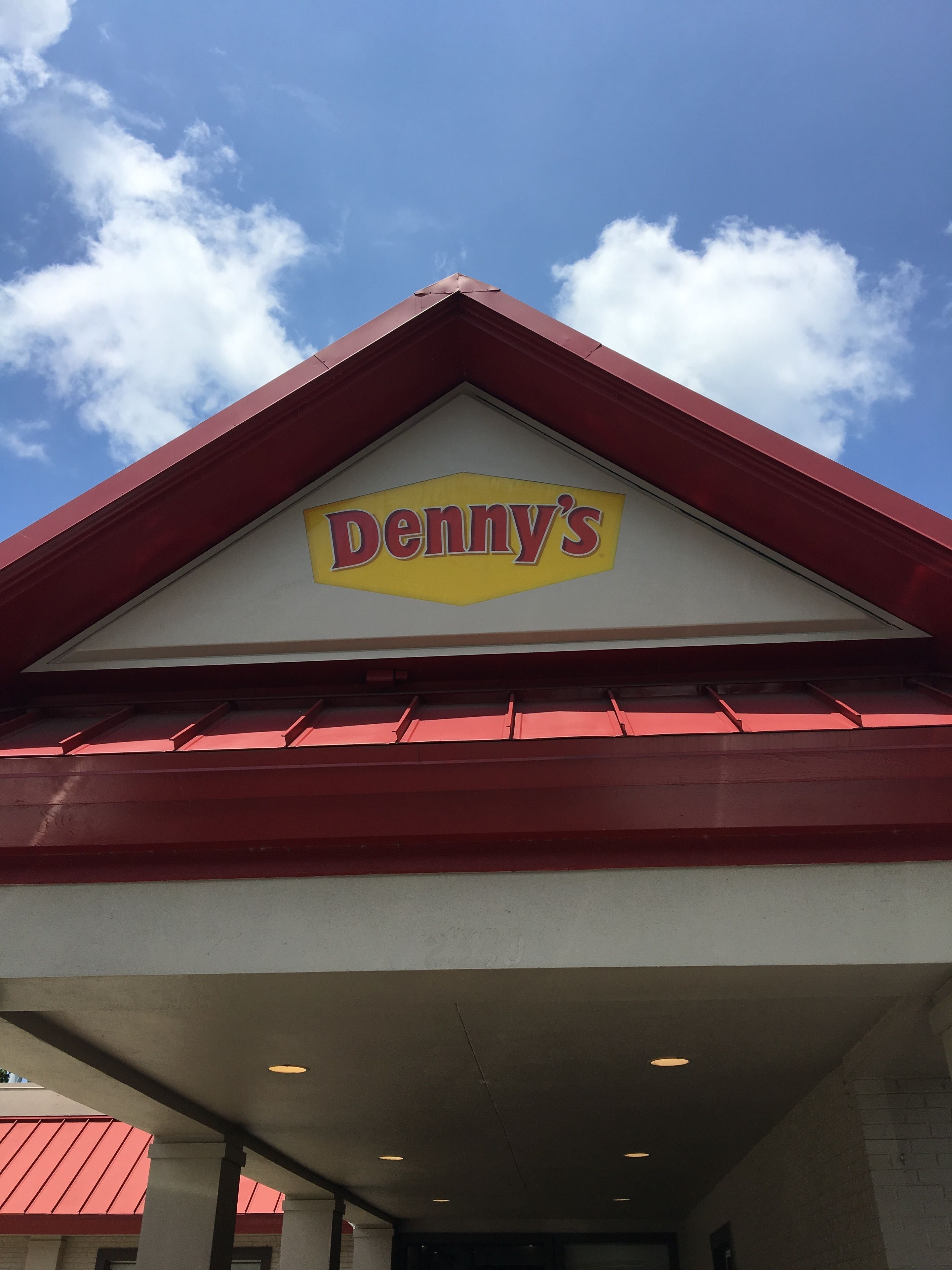The exterior of a Denny's restaurant with a red roof and a clear blue sky in the background.