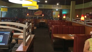 Interior de un restaurante con cabinas y mesas, una caja registradora y un letrero de 'Denny's'.
