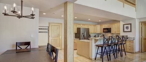 A spacious kitchen with wooden cabinets, a stainless steel refrigerator, and a microwave. There is a dining area with a wooden table and chairs.