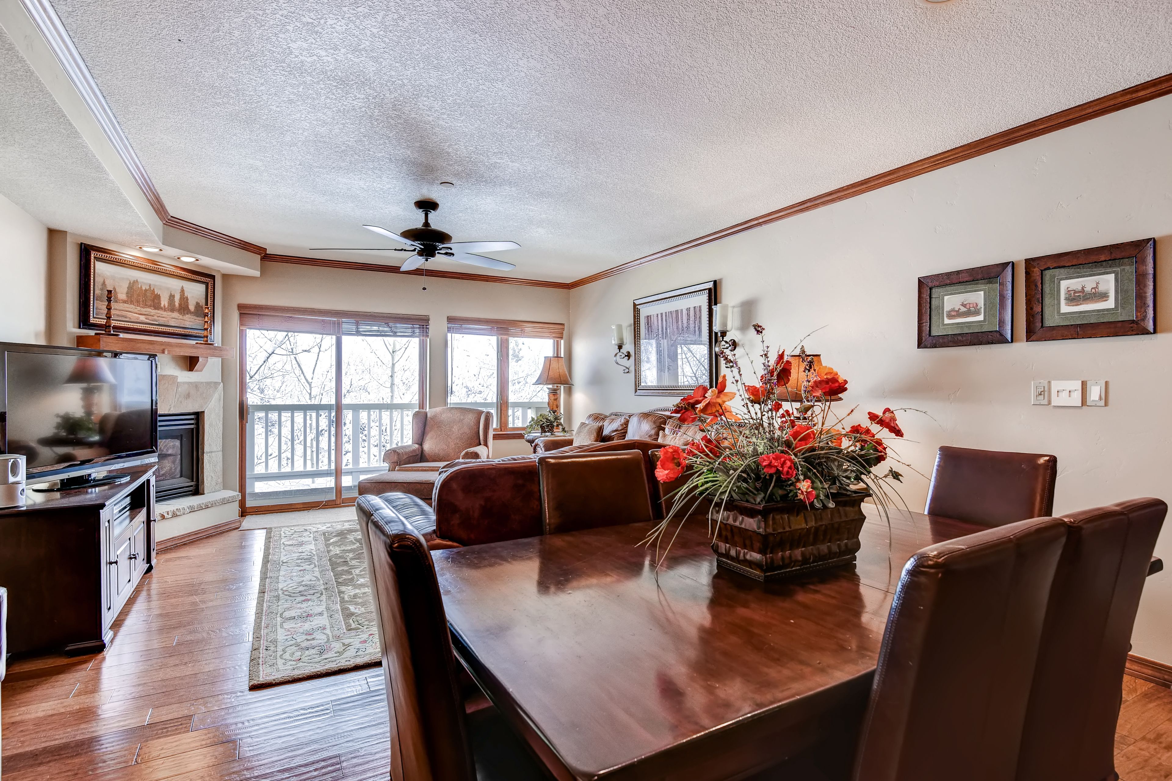 A spacious living room with a wooden dining table, comfortable seating, a fireplace, and a large window with a view.