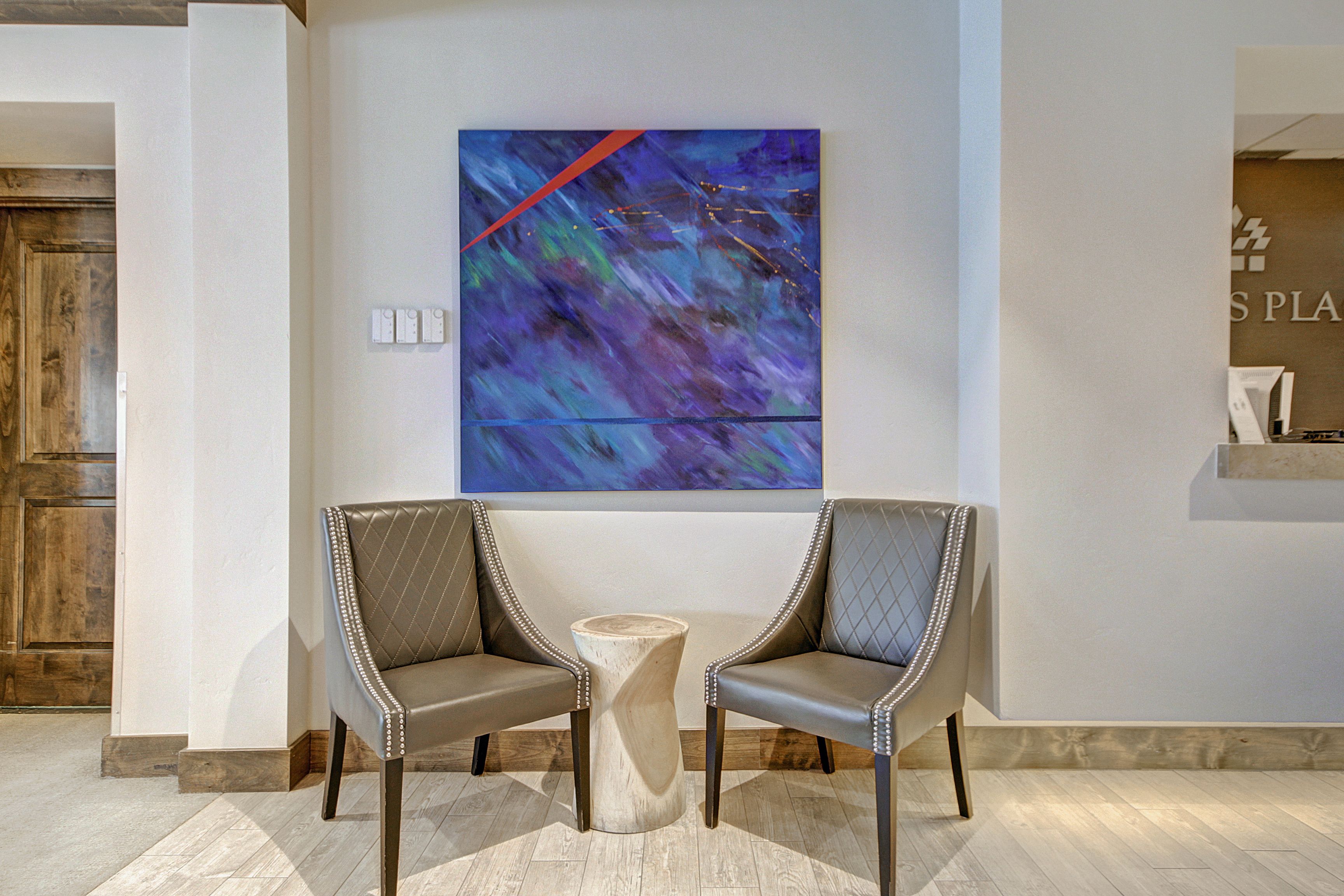 A modern lobby with two leather chairs, a wooden side table, and a large abstract painting on the wall.