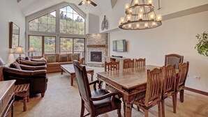 Un salón amplio con una gran mesa de comedor de madera, asientos cómodos, una chimenea y ventanas grandes que ofrecen vistas al exterior.