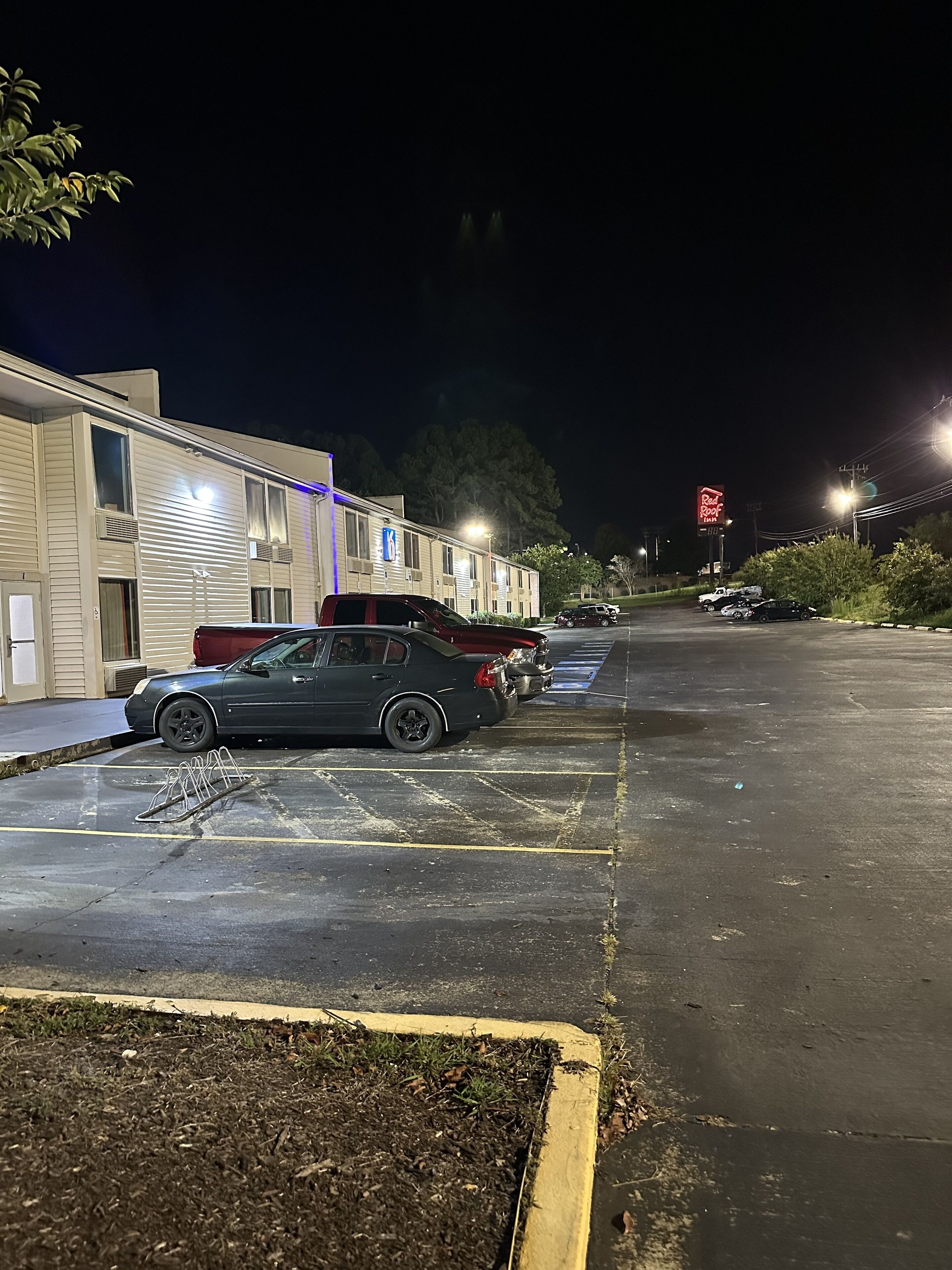 A parking lot with several cars, a motel building, and a Red Roof sign in the distance.