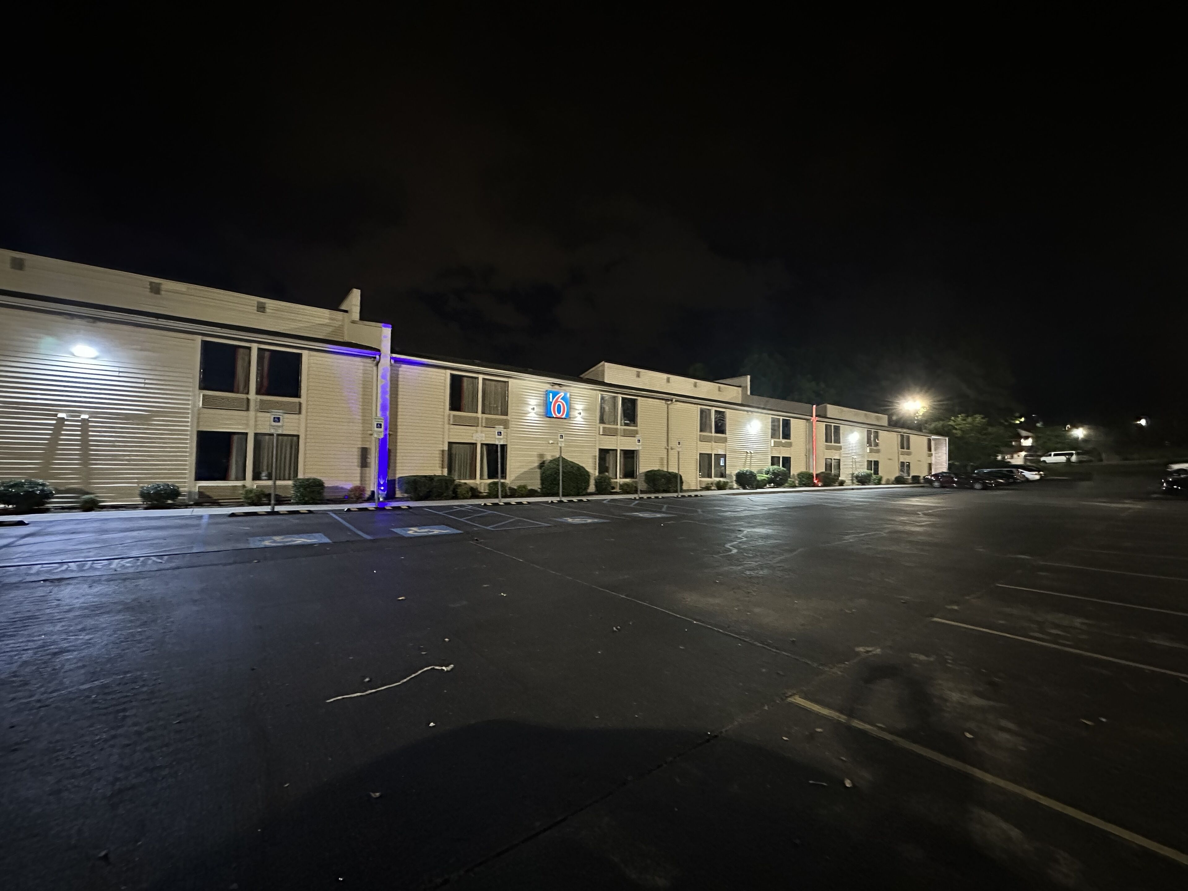 A motel with a parking lot, a 6-room sign, and a gated entrance.