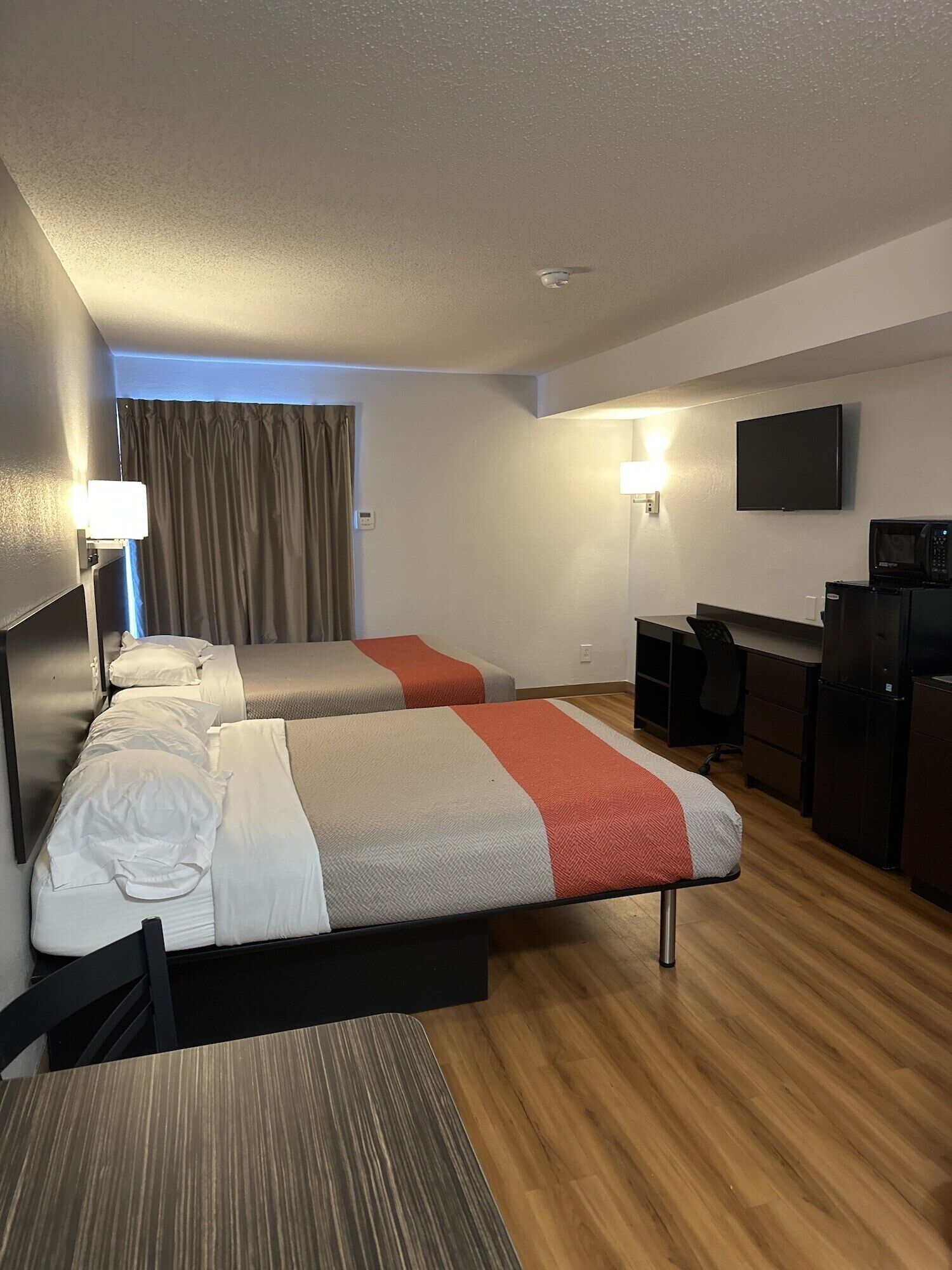 Habitación de hotel con dos camas, un escritorio, una silla, un televisor y un microondas.
