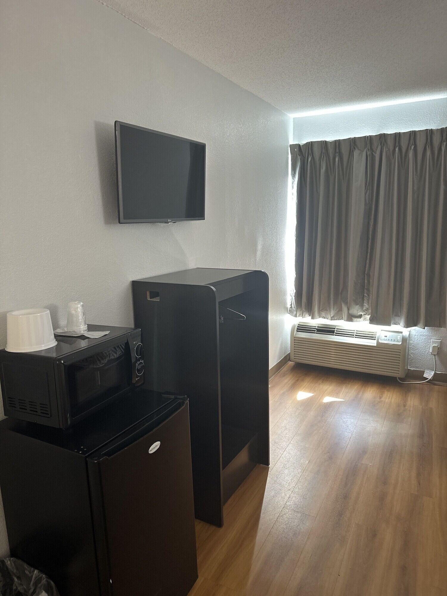 A compact room with a flat-screen TV mounted on the wall, a small black refrigerator, and a heater against the wall.