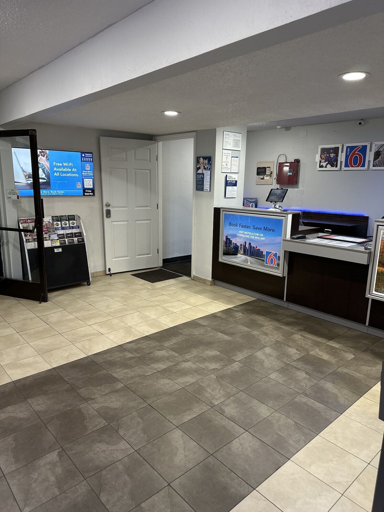 A reception area with a digital screen displaying Wi-Fi availability, a bookcase, a desk with a computer, and a wall-mounted display.