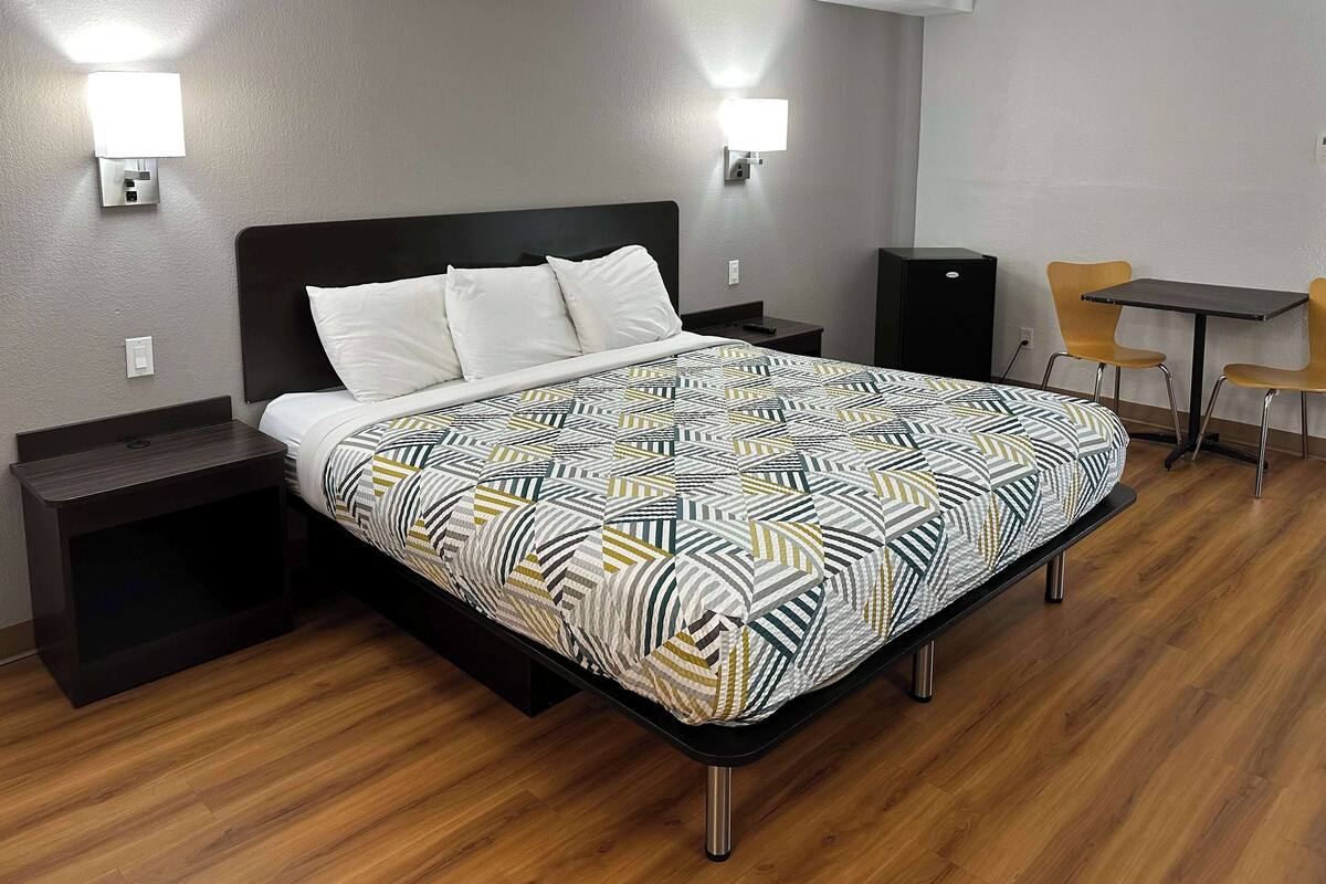 A hotel room with a bed, bedside tables, a desk with a chair, and wall-mounted lights.