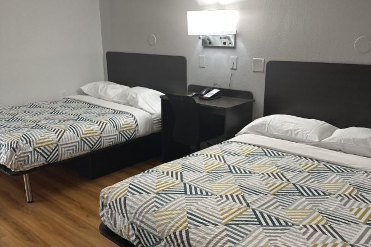 A hotel room with two beds, a desk with a phone, and a wall-mounted light.