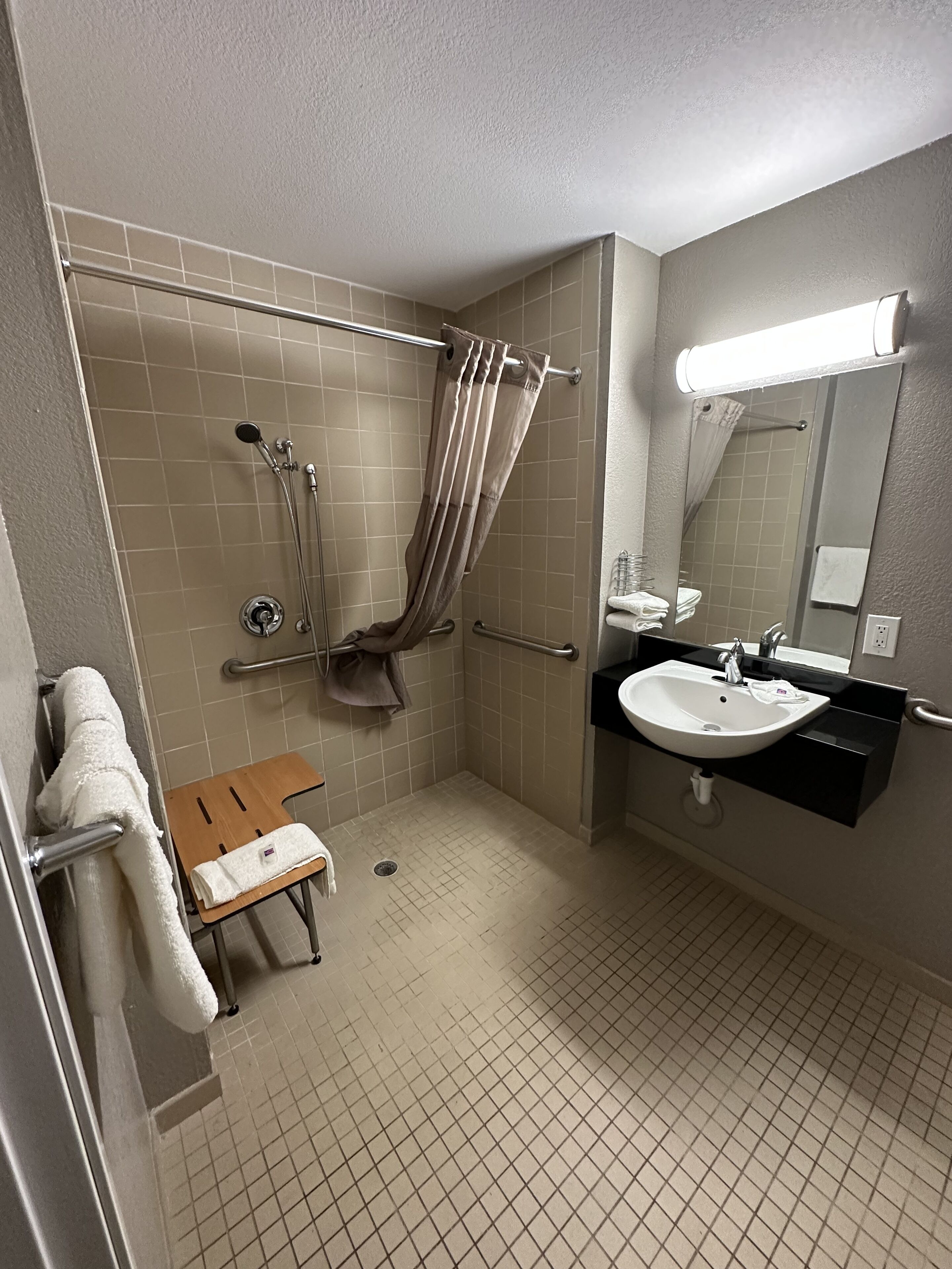 A small, tiled bathroom with a shower, a sink, and a mirror.
