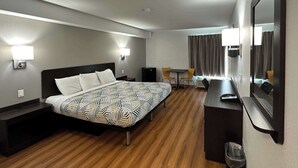 Ein Hotelzimmer mit Bett, Nachttischen, einem Schreibtisch, einem Sessel und einem Spiegel, sowie einem Fenster mit Vorhängen.