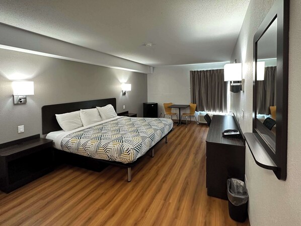 A hotel room with a bed, bedside tables, a desk, a chair, a mirror, and a window with curtains. - Motel 6 Greensboro, NC - Airport (Greensboro)