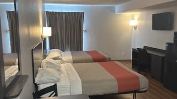 Ein Hotelzimmer mit zwei Betten, einem Schreibtisch, einem Stuhl, einem Flachbildfernseher und einer Lampe.