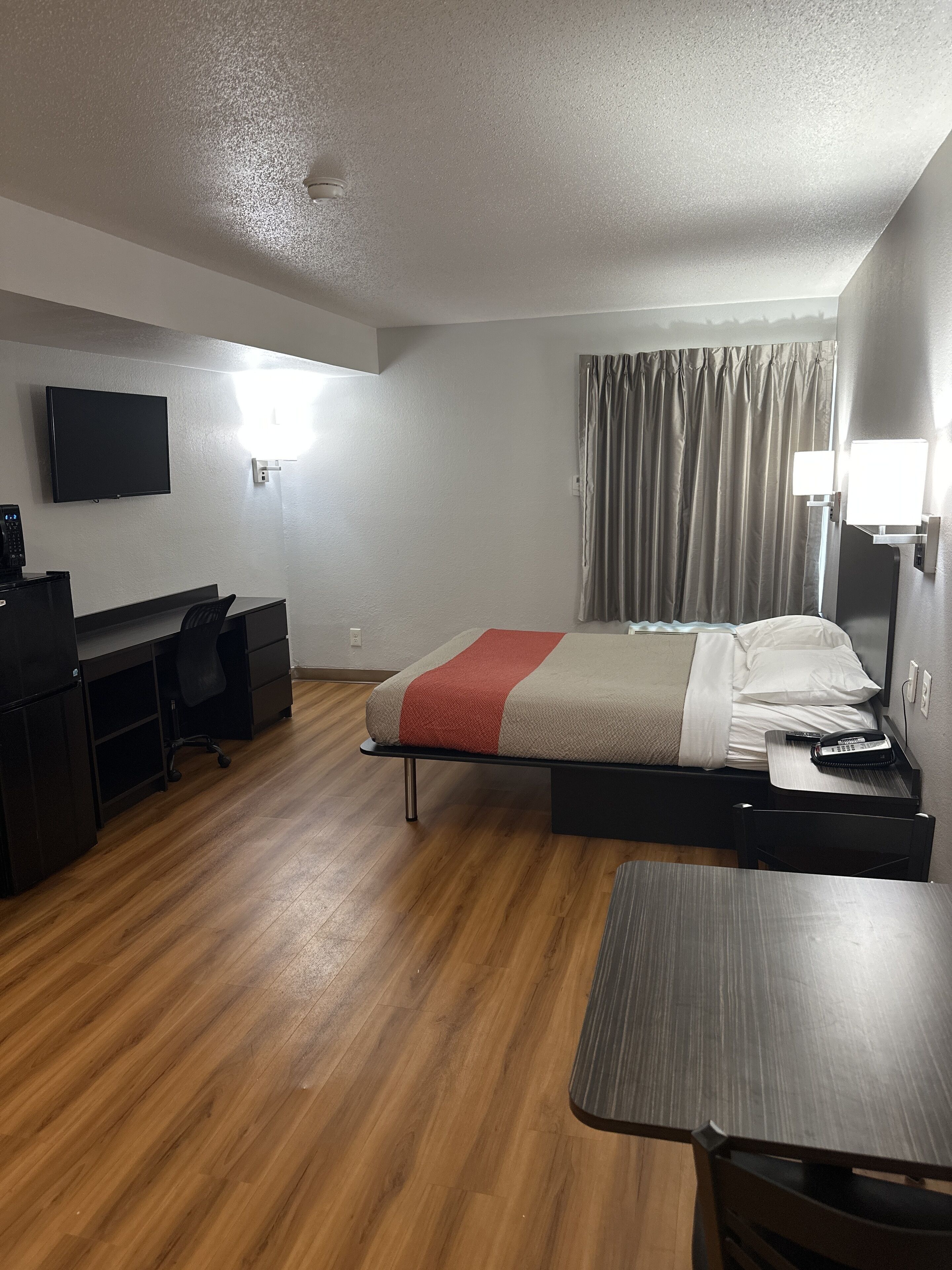 Ein Hotelzimmer mit Bett, Schreibtisch, Stuhl und einem Fernseher an der Wand.