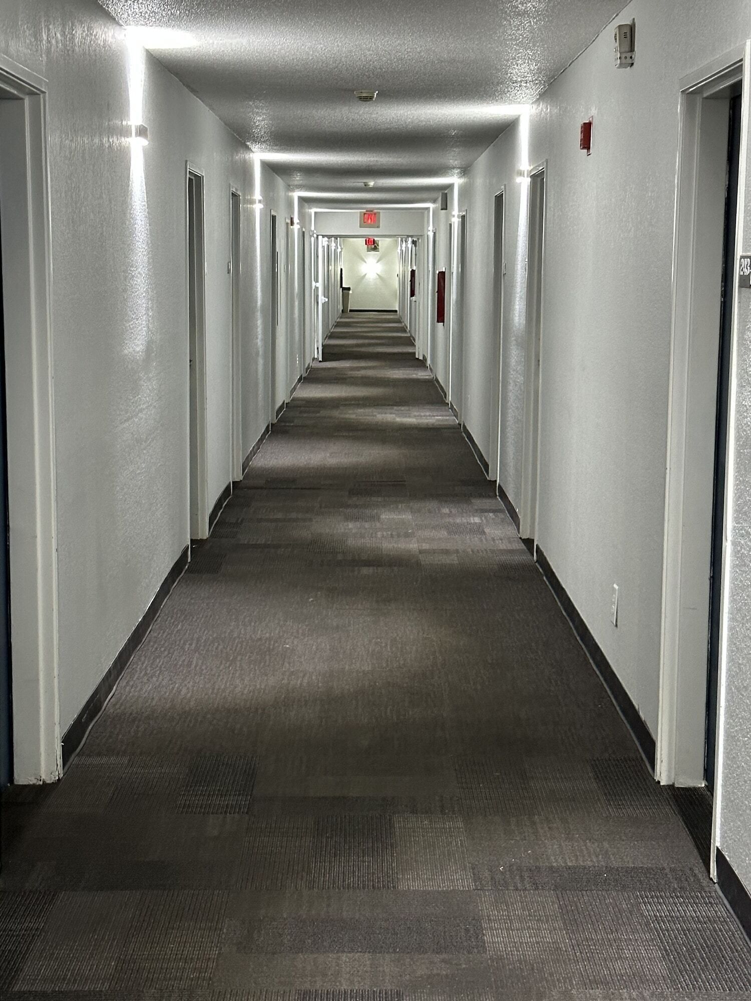 A long, narrow hotel corridor with carpeted floors and doors on both sides.