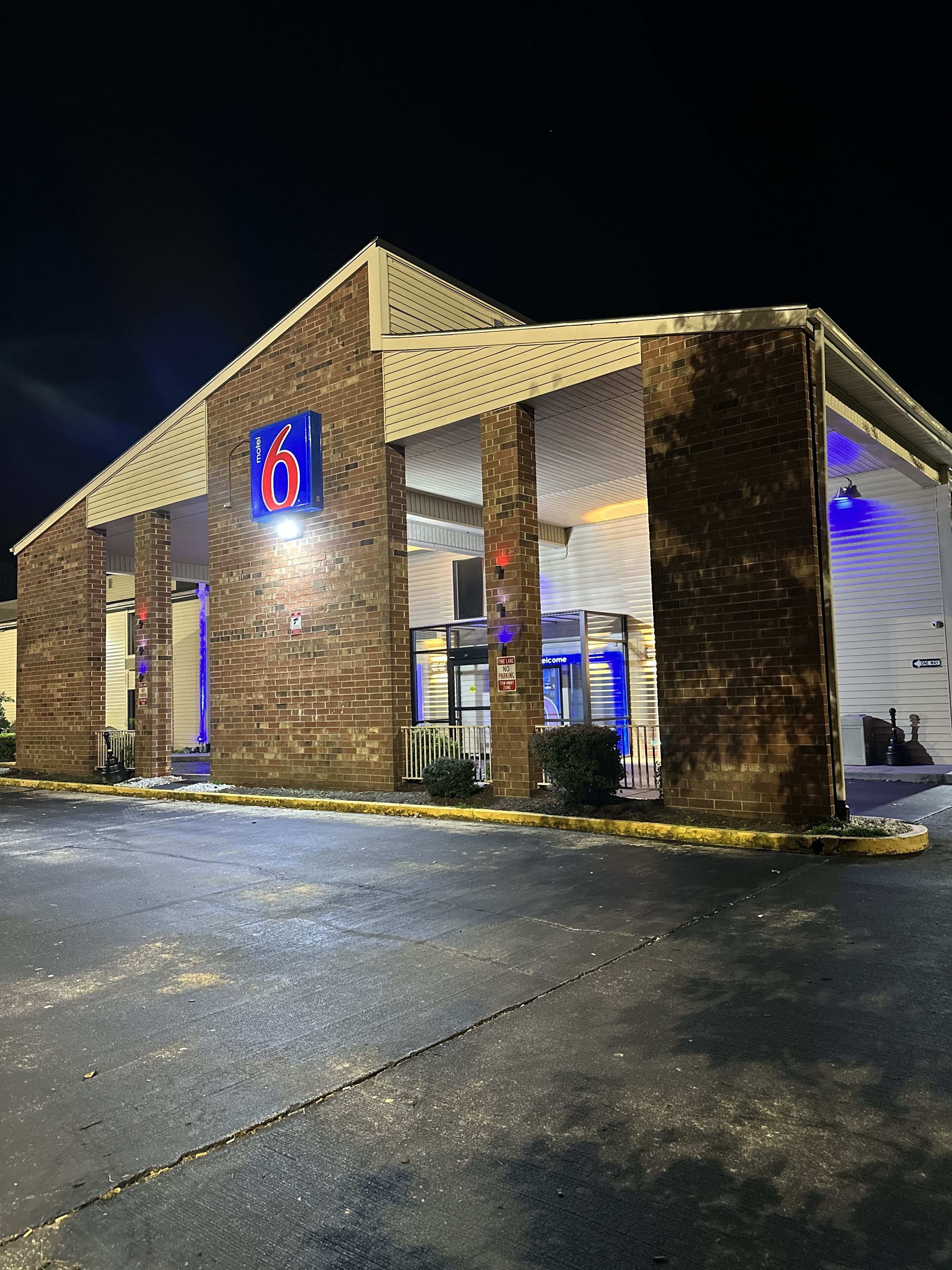 Un motel con un letrero que dice '6', zona de estacionamiento techada y entrada protegida por una reja.