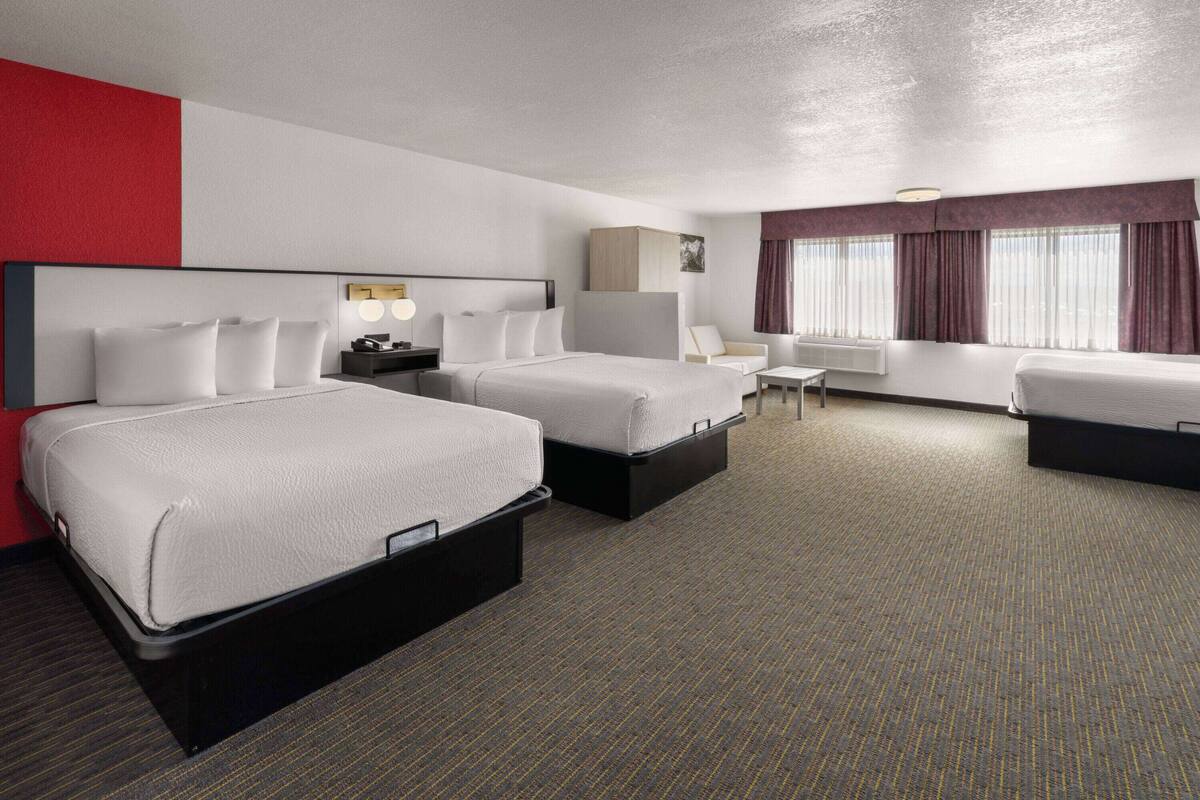 Ein Hotelzimmer mit zwei Betten, einem Schreibtisch, einem Stuhl und einem mit Vorhängen versehenen Fenster.