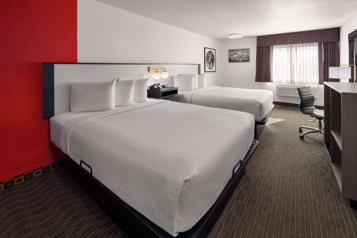 Ein Hotelzimmer mit zwei Betten, einem Schreibtisch, einem Stuhl und einem Fenster mit Vorhängen.